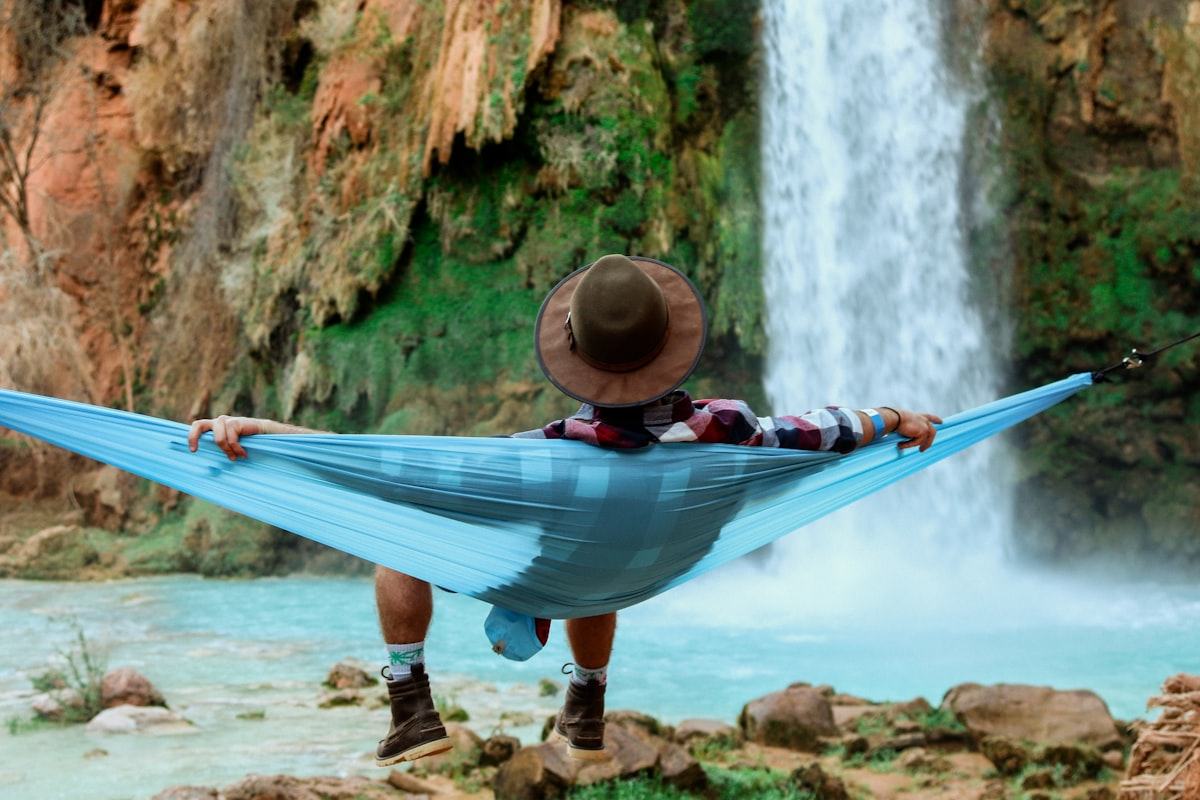 Pria bersantai di hammock di dekat air terjun